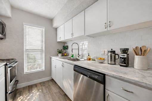 A kitchen with a stainless steel dishwasher and white cabinets. at Infinity on the Landing Apartments , Apartments, Euless, TX