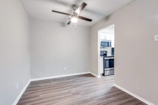 A room with a ceiling fan and a kitchen in the background at Infinity on the Oaks Apartments, Dallas, TX, 75231