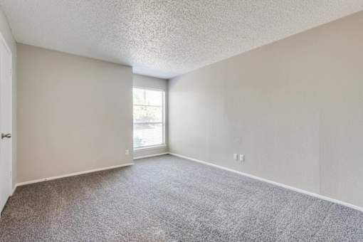 A room with a carpeted floor and a window letting in light at Infinity on the Oaks Apartments, Dallas 75231