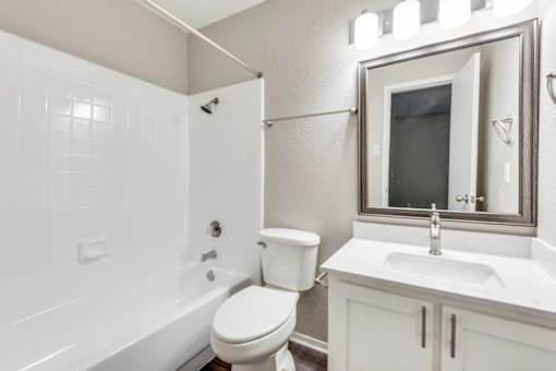A white bathroom with a toilet, sink, and bathtub at Infinity on the Oaks Apartments, Texas