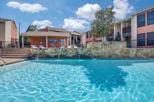 A swimming pool in front of a building with a stone wall and a tre at Infinity on the Oaks Apartments , Dallas, TXe