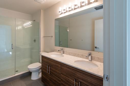 A bathroom with a toilet, sink, mirror, and shower.