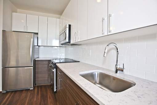 A modern kitchen with a stainless steel refrigerator and a sink with a marble countertop.