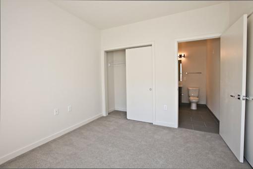 A white room with a carpeted floor and a toilet in the hallway.
