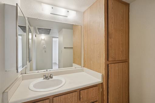 A bathroom with a sink, mirror, and wooden cabinet.