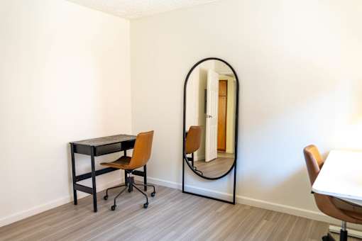 A black desk with a chair and a mirror in a room.
