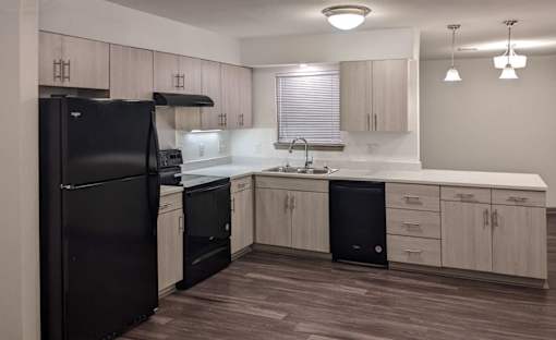A black refrigerator is in a kitchen with wooden floors and white walls.