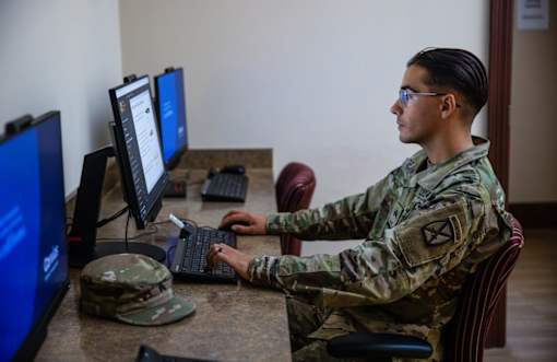 A man in military uniform is working on a computer.