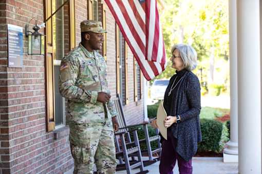 A man in military uniform stands outside a building talking to a woman.