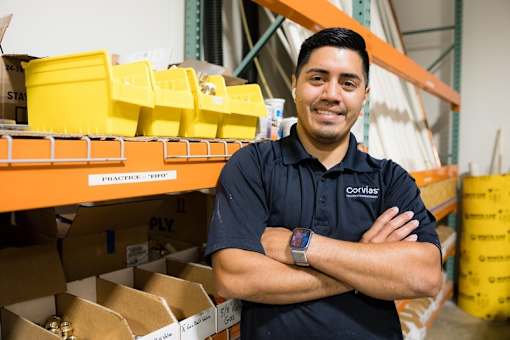 A man in a black shirt with his arms crossed in front of a shelf with boxes and containers.