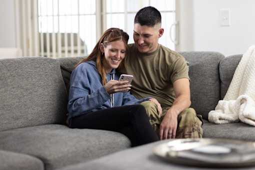 A man and a woman are sitting on a grey couch, with the woman looking at her phone.