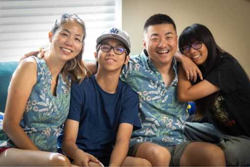 A group of four people wearing matching blue shirts with a pattern of white birds and green leaves.