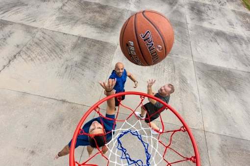 A basketball is in mid-air as it approaches two players who are reaching for it.