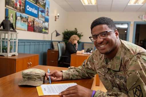 A soldier in uniform is signing a document at a desk.
