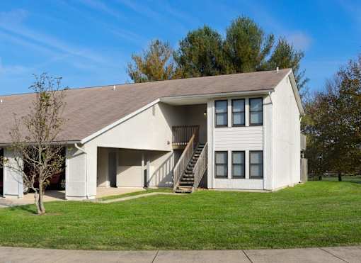 A white building with a brown roof and a tree in front.