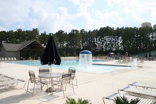 A poolside table with chairs and an umbrella is in front of a pool with a waterfall.