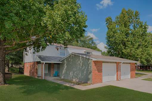 A house with a grey roof and a brick chimney is surrounded by green trees.