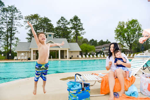 A child jumps into a swimming pool while a woman and a baby watch.