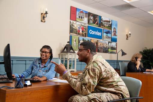 A man in military uniform is talking to a woman in a denim jacket in an office setting.