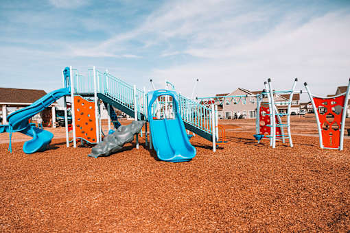 A playground with a blue slide and orange and grey climbing structures.