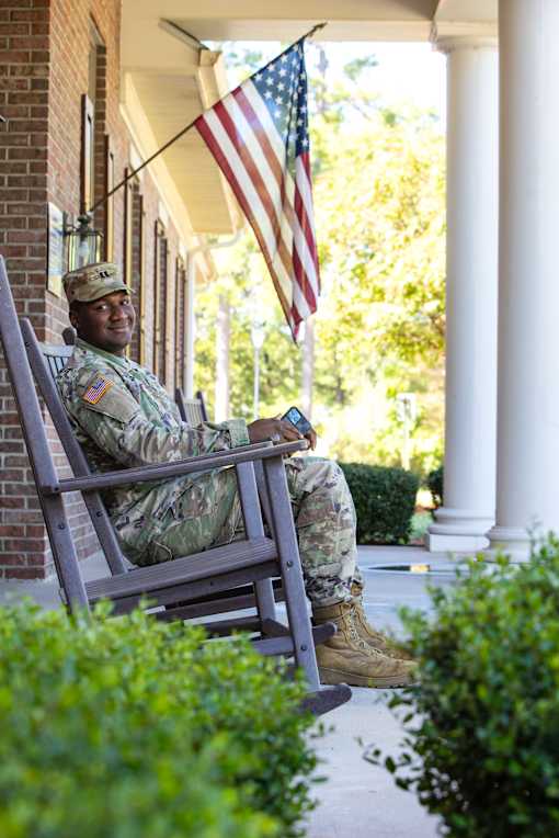 A soldier in uniform sits on a porch swing.