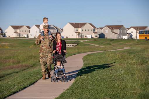 A man in military uniform pushes a stroller with a child in it while a woman walks beside them.