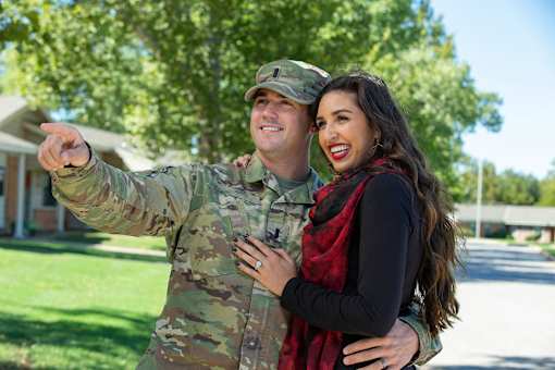 A man in military uniform points at something while standing next to a woman.