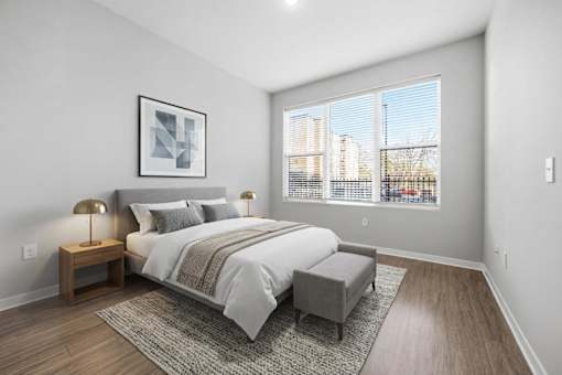 A bedroom with a large bed, a bench, and a window overlooking a cityscape.