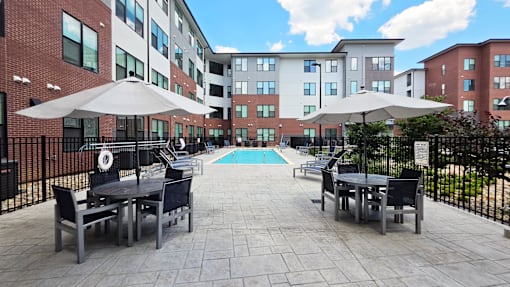 A patio with tables and chairs and umbrellas is surrounded by a black fence.