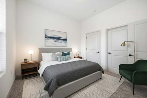 A bedroom with a large bed, a green chair, and a painting on the wall.