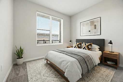 A bedroom with a large bed, a potted plant, and a framed picture on the wall.