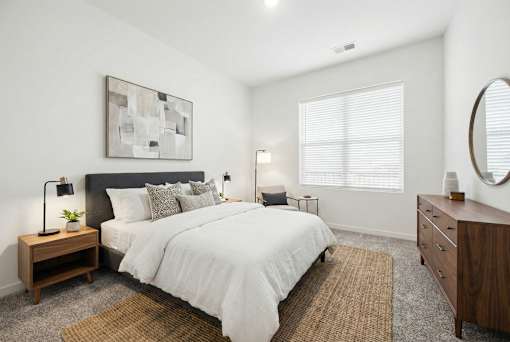 A bedroom with a large bed, a nightstand with a lamp, and a painting on the wall.