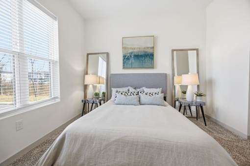 A bedroom with a large bed, two lamps, and a painting on the wall.