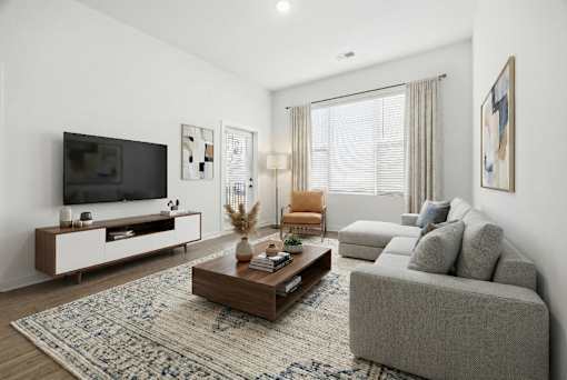 A modern living room with a grey sofa, a wooden coffee table, and a television on a white cabinet.