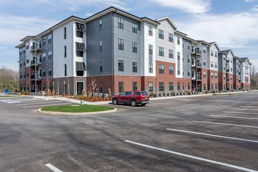 A red car is parked in a parking lot in front of apartment buildings.