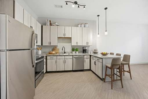 A kitchen with a refrigerator, oven, sink, and a chair.
