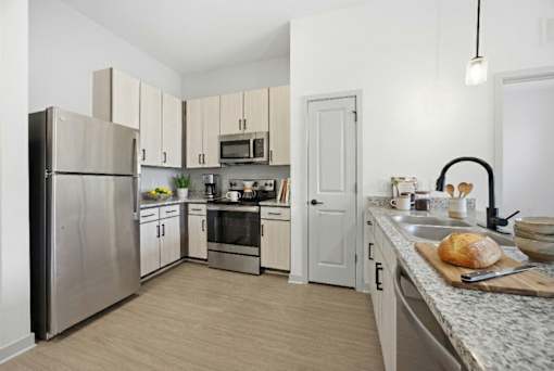 A kitchen with a refrigerator, oven, microwave, sink, and cabinets.