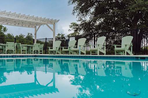 A pool with a white canopy and green chairs.