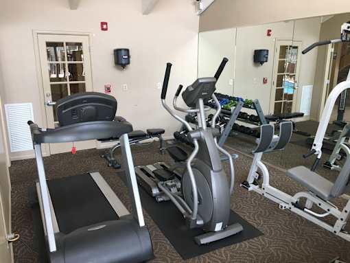 A gym with a treadmill, elliptical, dumbbells, and other exercise equipment.