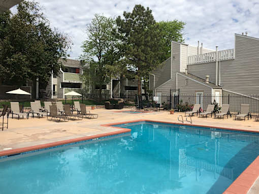 A swimming pool surrounded by chairs and trees.