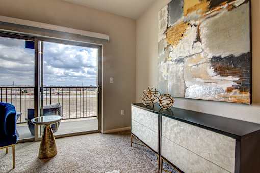 A room with a large painting on the wall and a view of the outside through a sliding glass door.