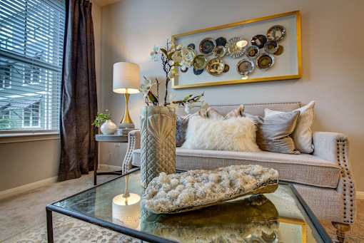 A living room with a grey couch, a glass table, and a large picture frame on the wall.