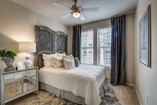 A bedroom with a large bed, a ceiling fan, and a window with curtains.