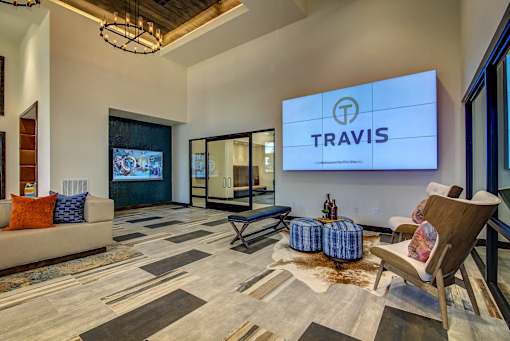 A living room with a couch, chairs, and a TV displaying the word "TRAVIS".