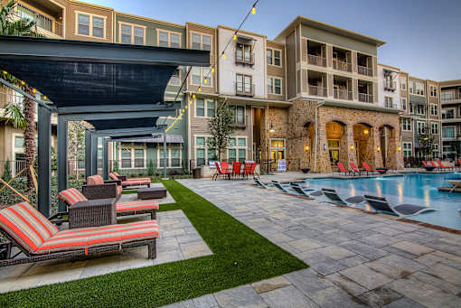 A pool area with lounge chairs and a building in the background.