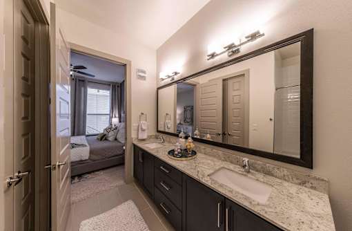 A bathroom with a sink, mirror, and a bedroom in the background.