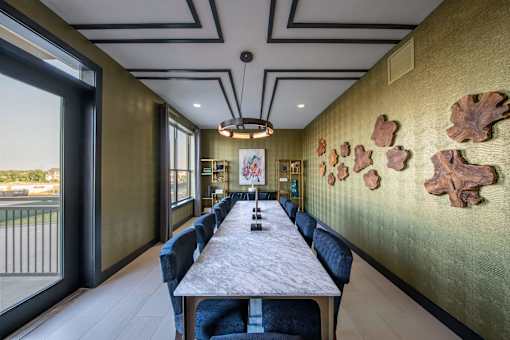 A long table with chairs and a wall with leaves on it.