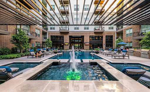 A large fountain in the middle of a pool surrounded by lounge chairs.