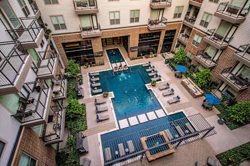 A large swimming pool surrounded by lounge chairs and balconies of apartment buildings.