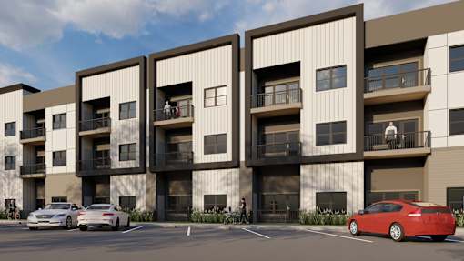A red car is parked in front of a building with three balconies.